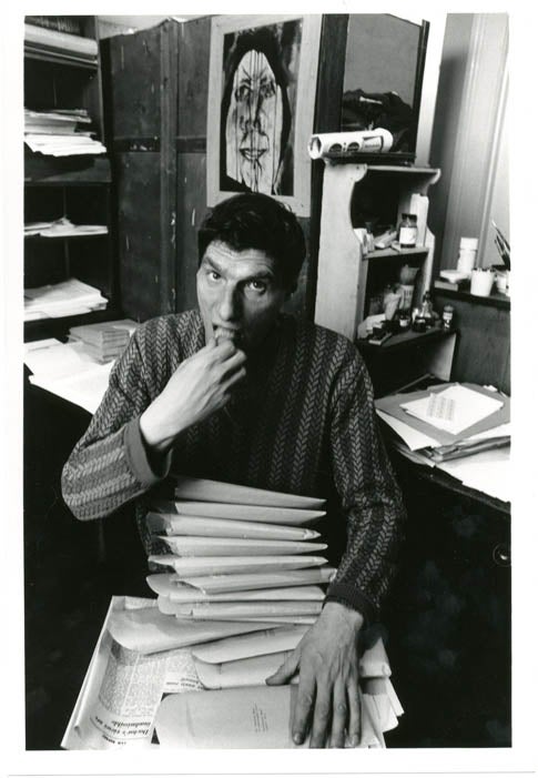 Item #39345 An original b/w photograph by John Hopkins of Alexander Trocchi sitting at his desk at 6 St. Stephen's Gardens, Notting Hill, taken either a moment before or after the image above, c. late 1964.